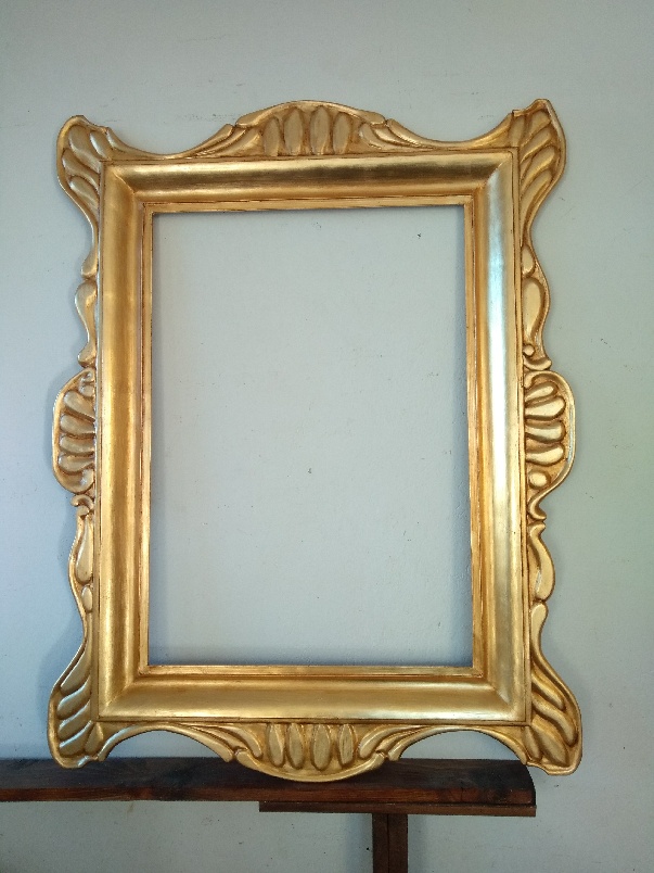 golden frame laying next to the wall on a wooden shelf